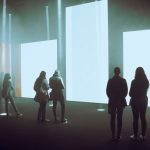 Visitantes exploram uma exposição de arte digital imersiva diante de grandes telas iluminadas.