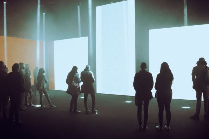 Visitantes exploram uma exposição de arte digital imersiva diante de grandes telas iluminadas.