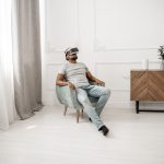 Homem sentado em uma poltrona usando óculos de realidade virtual em um ambiente interno.