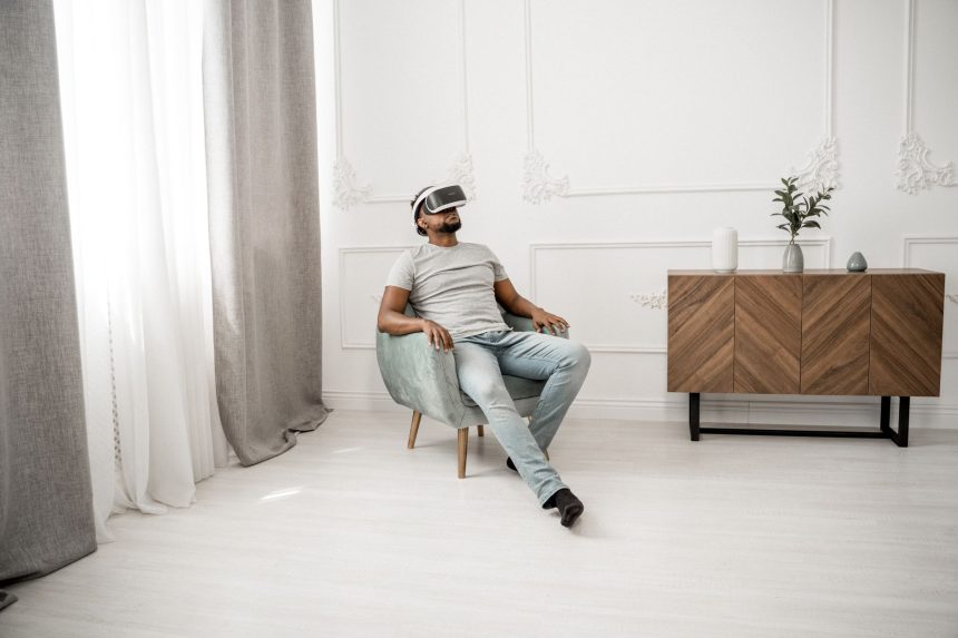 Homem sentado em uma poltrona usando óculos de realidade virtual em um ambiente interno.