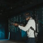 Homem usando um headset de realidade virtual e uma arma simulada durante uma partida de videogame.
