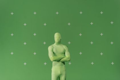 Pessoa usando traje verde diante de uma tela de chroma key marcada em um estúdio de produção audiovisual.