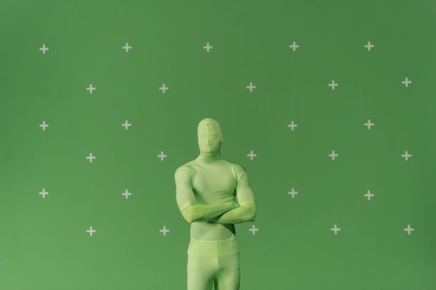 Pessoa usando traje verde diante de uma tela de chroma key marcada em um estúdio de produção audiovisual.
