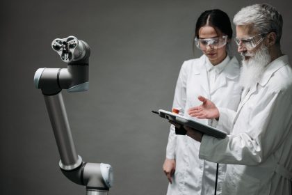 Pesquisadores de jaleco e óculos de proteção trabalham com um braço robótico em um laboratório.