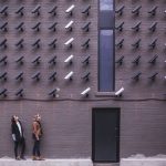 Mulheres observam uma parede urbana coberta por diversas câmeras de segurança.