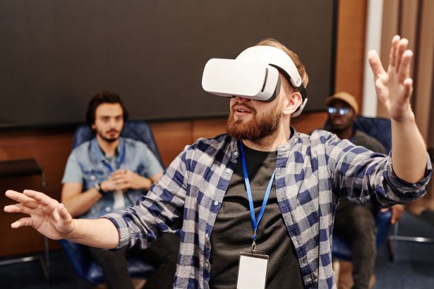 Homem usa um headset de realidade virtual em ambiente interno, enquanto outras pessoas aparecem ao fundo.