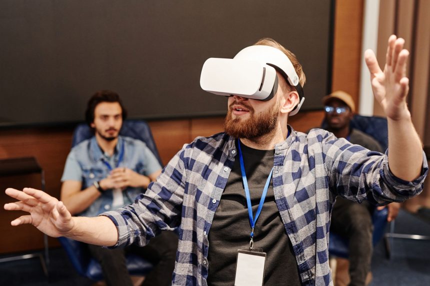 Homem usa um headset de realidade virtual em ambiente interno, enquanto outras pessoas aparecem ao fundo.