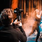 Fotógrafo registra uma apresentação de dança em um palco, com o movimento dos artistas em destaque.