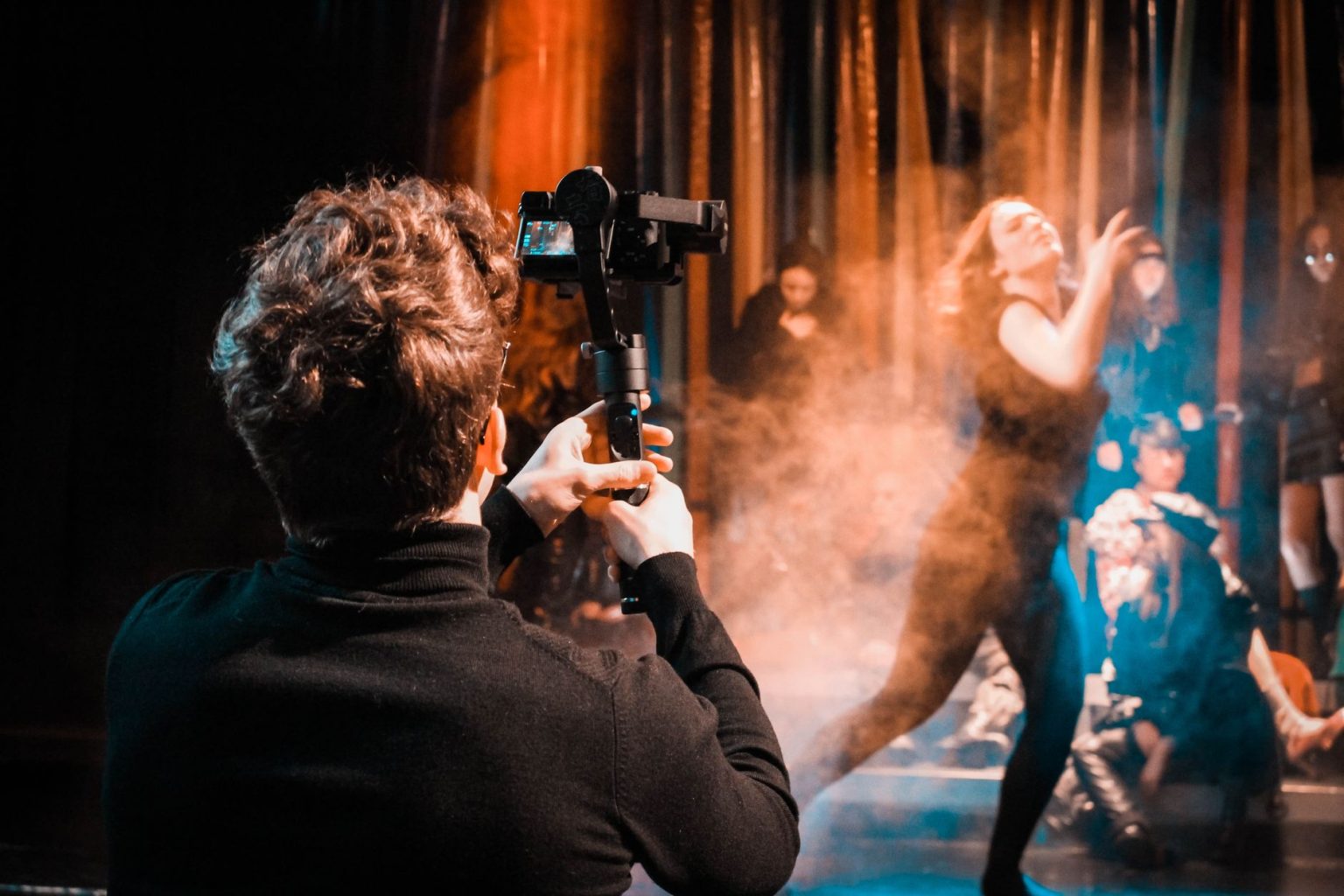 Fotógrafo registra uma apresentação de dança em um palco, com o movimento dos artistas em destaque.