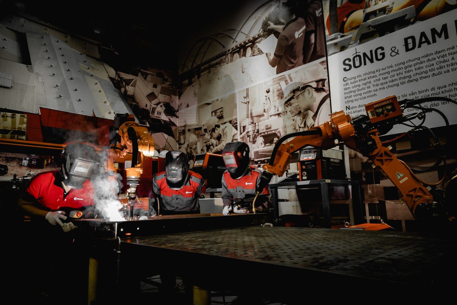 Três trabalhadores usando equipamentos de proteção atuam com robôs em uma oficina industrial de alta tecnologia.